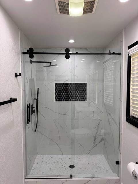 Completed walk-in shower with marble-look tile, black fixtures, and glass enclosure.